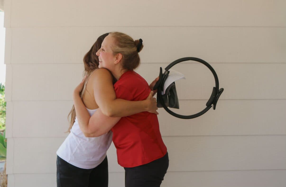 Tracey hugging a client who is holding a Pilates ring