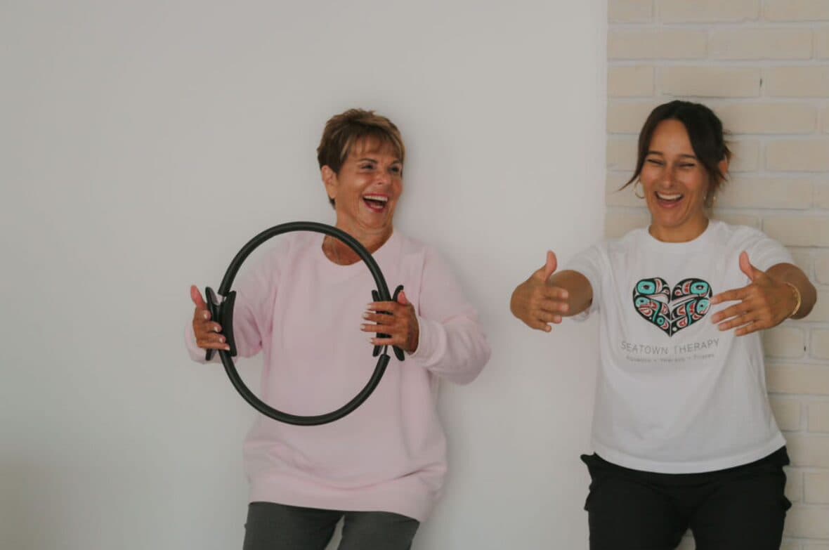 Tracey and a client laughing as the client holds a Pilates ring during a therapeutic exercise session